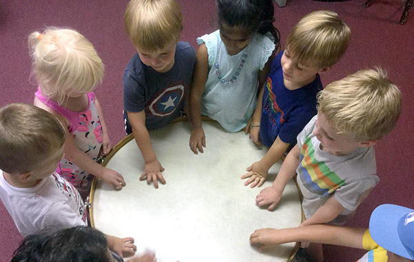 Preschoolers playing a large hand drum.